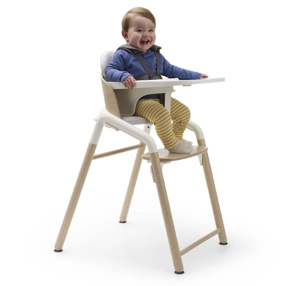 Bugaboo Giraffe Complete High Chair Set with light wood frame and white tray; baby in blue top sits securely.