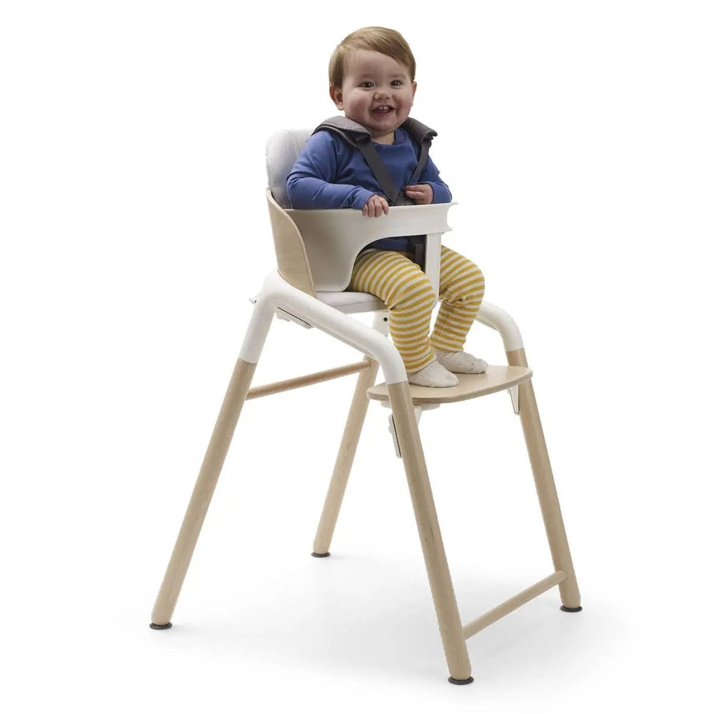 Bugaboo Giraffe Complete High Chair Set with light wood legs and beige tray, child securely strapped in.