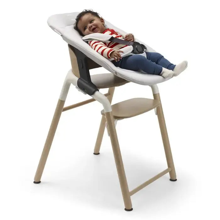 Bugaboo Giraffe Newborn Set high chair in white cushion and beige wood frame, baby secured with safety harness.
