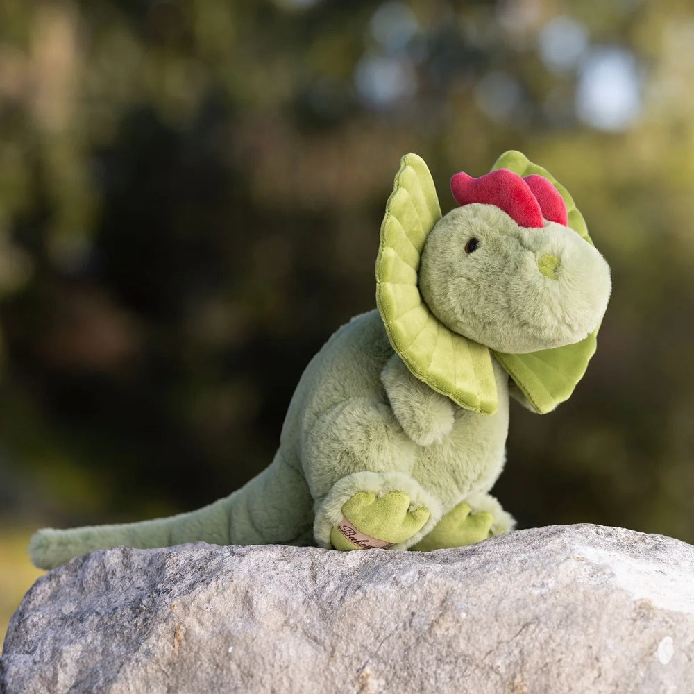 Bukowski Bears Dilo plush dinosaur sits on a rock with soft green fur, lime frill, and pink-red crest.