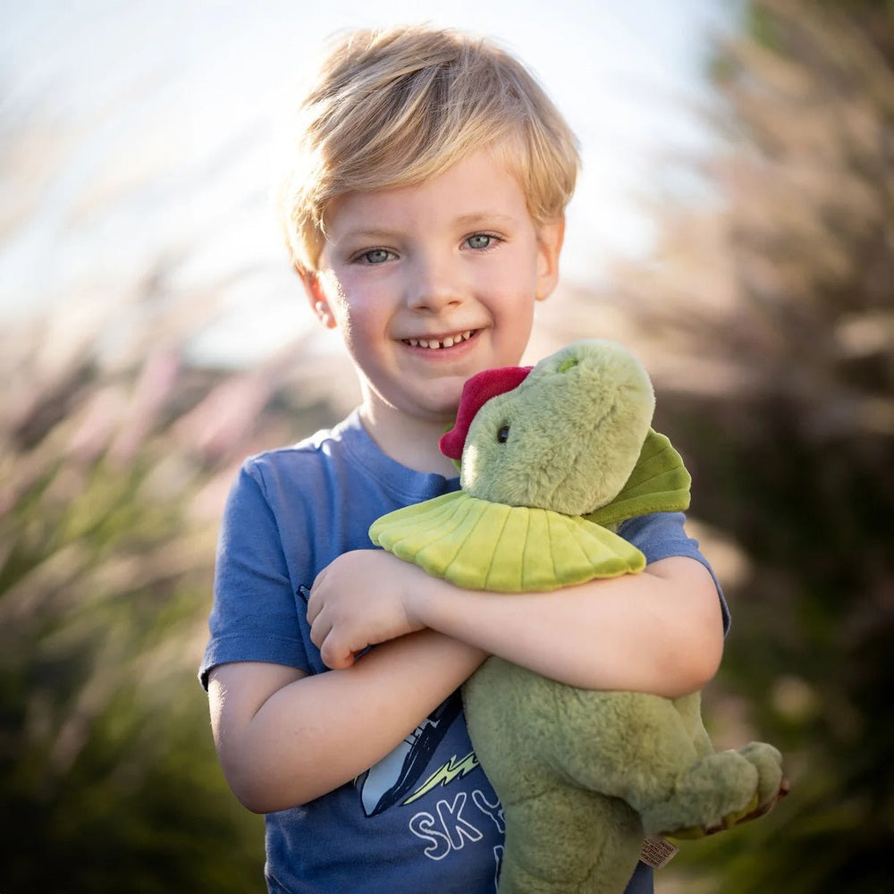 Bukowski Bears Dilo stuffed animal held by a smiling child outdoors, green dinosaur with red crest and lime scarf.