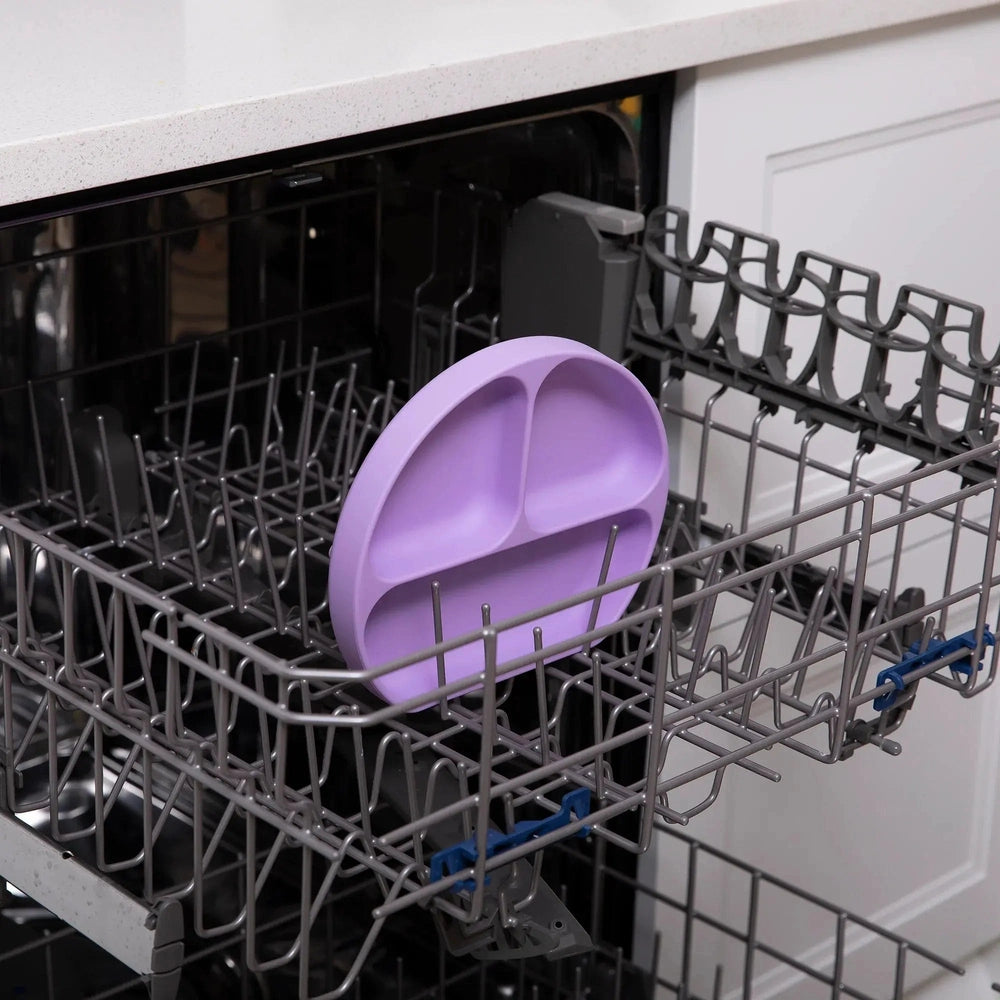 Bumkins Silicone Grip Dish purple sits in a dishwasher rack, showing its non-slip silicone grip for toddler meals.