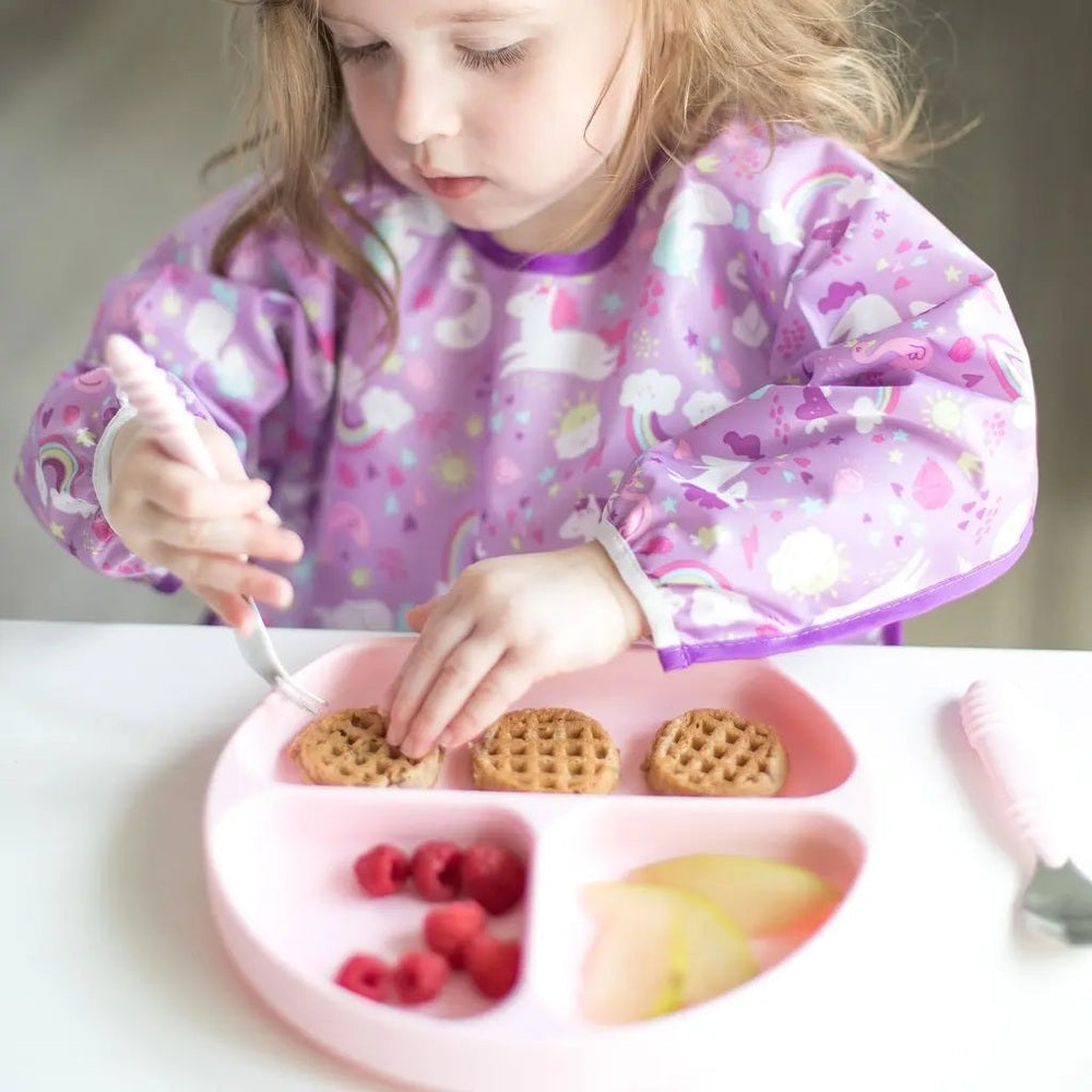 Bumkins Silicone Grip Dish pink divided baby feeding plate with non-slip grip, as a girl uses a fork to