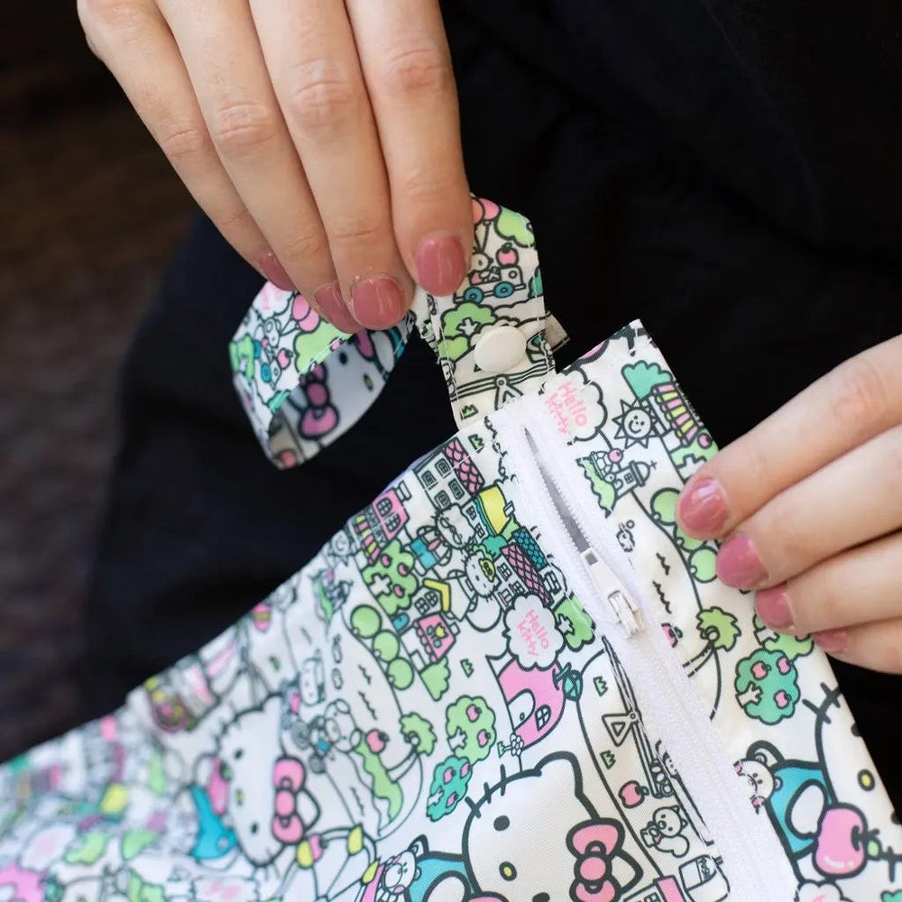 Bumkins Wet Bag in bright cartoon print; hands unzip the white zipper along the bag’s seam.