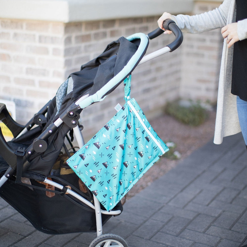 Bumkins wet bag, turquoise with teal triangle pattern, attached to stroller handle during outdoor parenting.