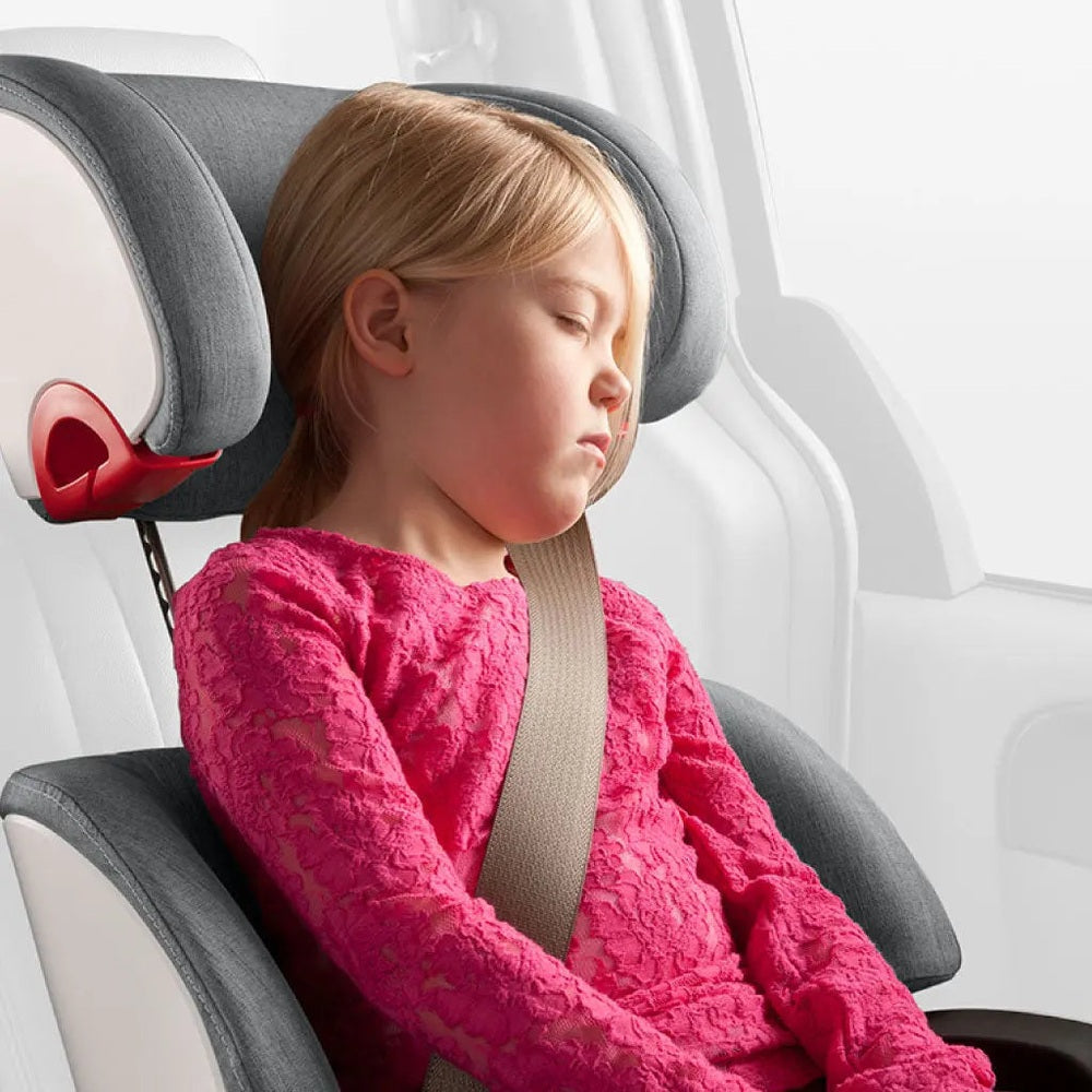 Clek Boost Seat Oobr booster in gray car interior; child in pink lace dress buckled with beige belt across lap.
