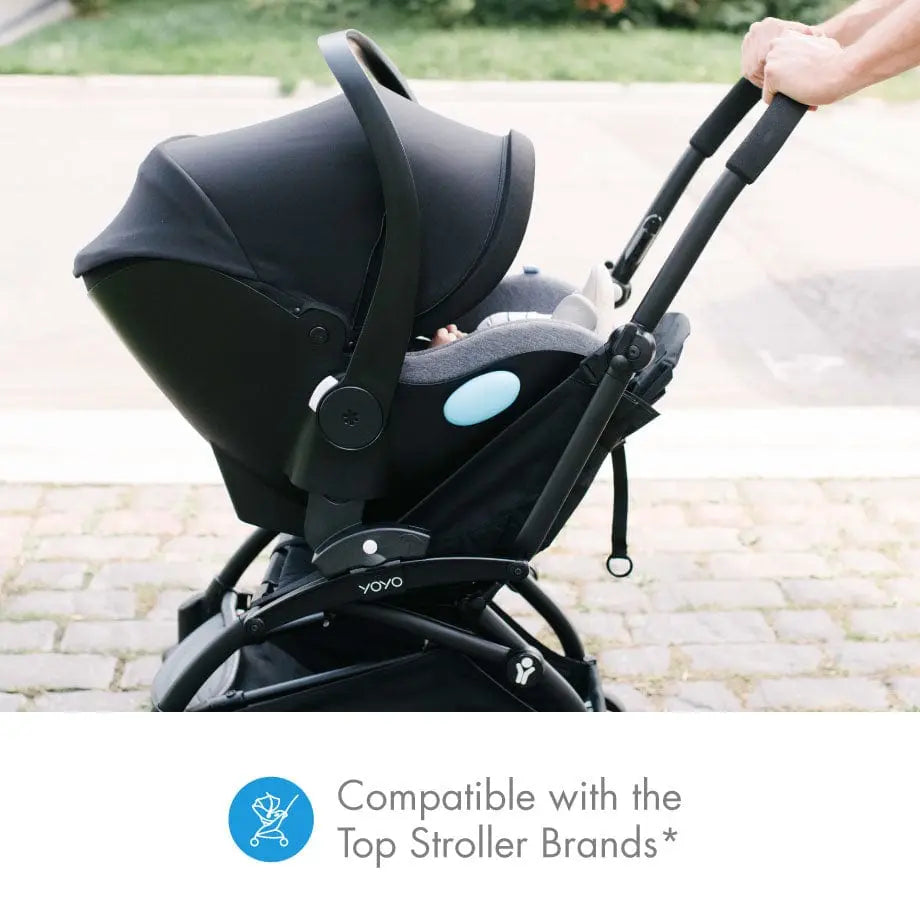 Clek Liing infant car seat mounted on a black stroller frame; handle gripped by a parent, blue accent badge visible.