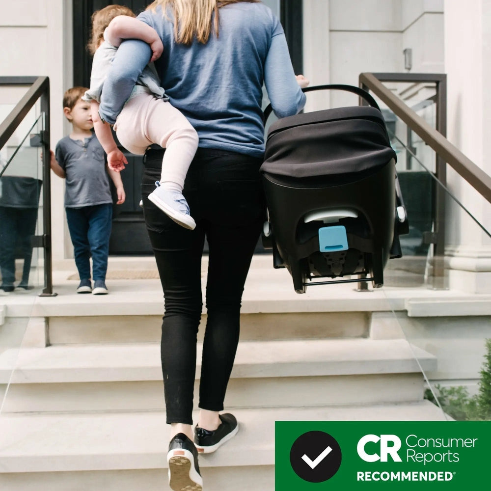 Clek Liing infant car seat in black with blue latch, carried by parent beside a stroller on steps.