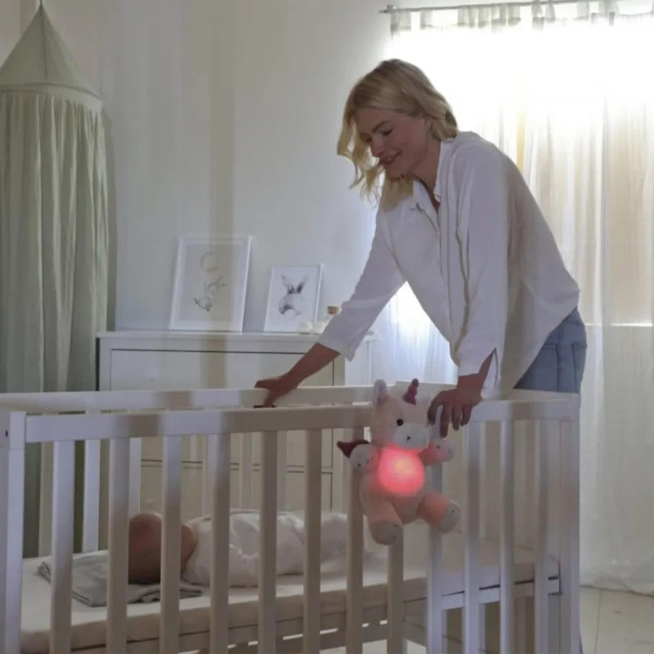 Cloud B Love Light Lily the Unicorn plush with glowing pink heart hanging from a white crib