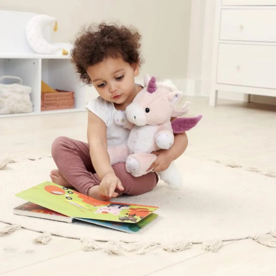 Cloud B Love Light Lily the Unicorn plush in pink with purple wings; child sits reading a colorful book.