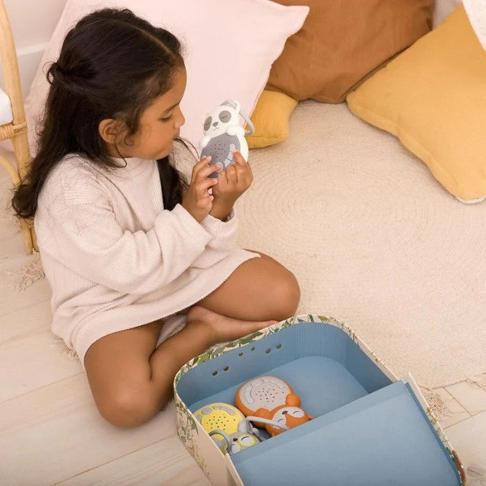 Cloud B Sweet Dreamz On the Go Panda plush sleep aid, gray and white, held by a child beside a toy box.