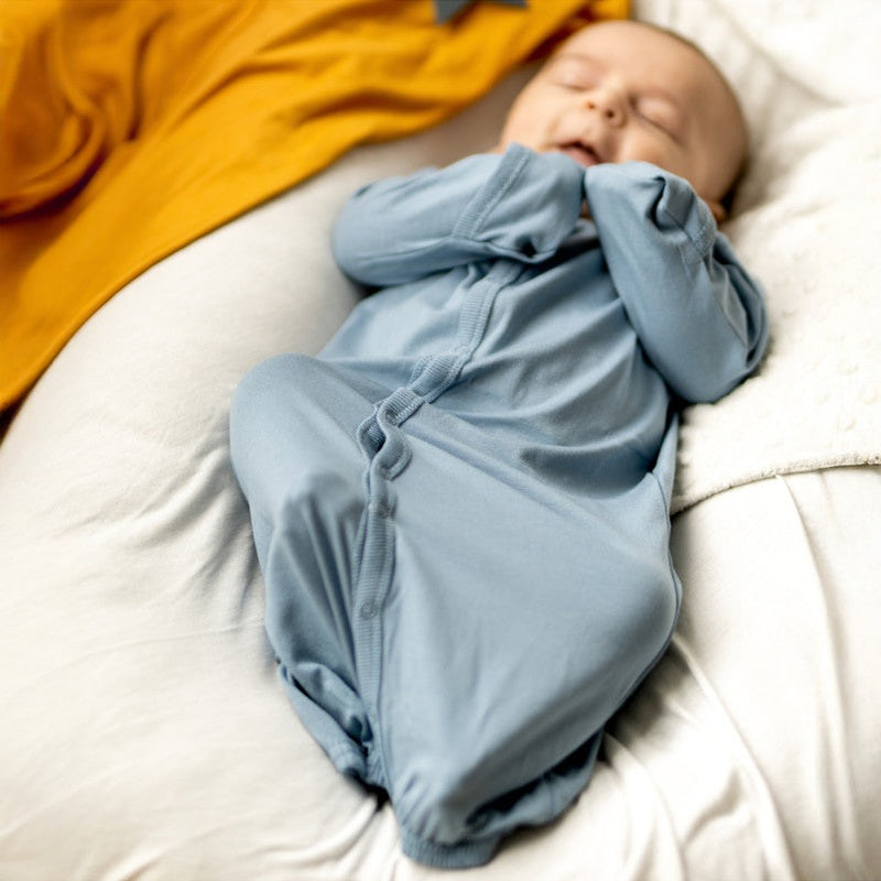 Coccoli Infant Cotton TENCEL™ Modal Converter Steel Blue onesie; sleeping baby on a cream sofa with an orange blanket.