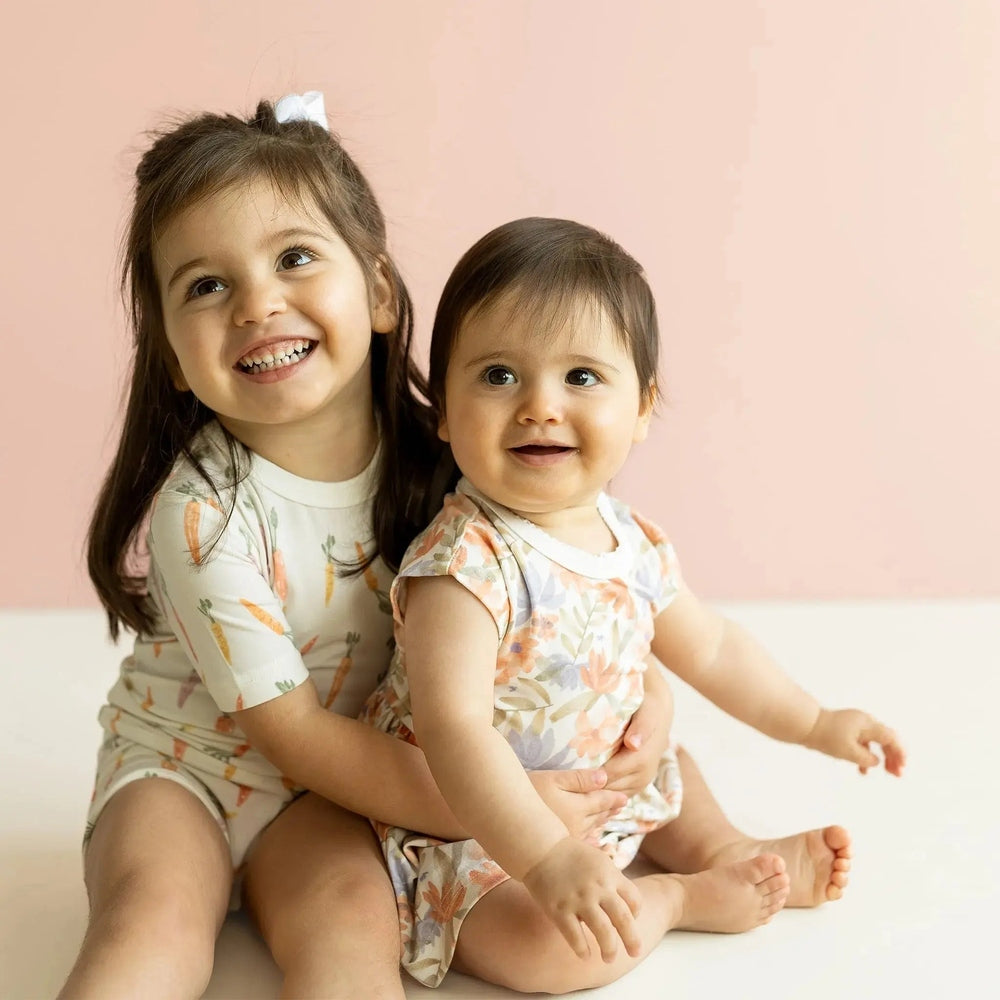Coccoli Kid Cotton TENCEL™ Modal Short Sleeve Pajama Carrots On Cream; two happy children wear matching cream carrot-print pajamas.