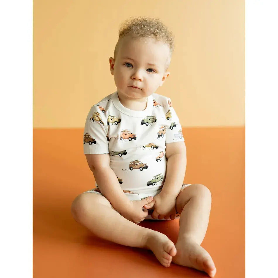 Coccoli Kid Jeeps Cotton TENCEL™ Modal Short Pajamas; white jeep-printed romper, baby sits cross‑legged showing comfy fit.