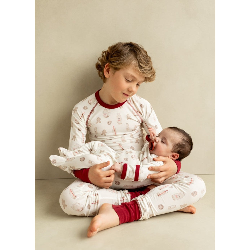 Coccoli Kid long-sleeved Cotton TENCEL™ Modal Pyjama Cookies On Cream; a boy cradles a baby in matching sleepwear with red cuffs.