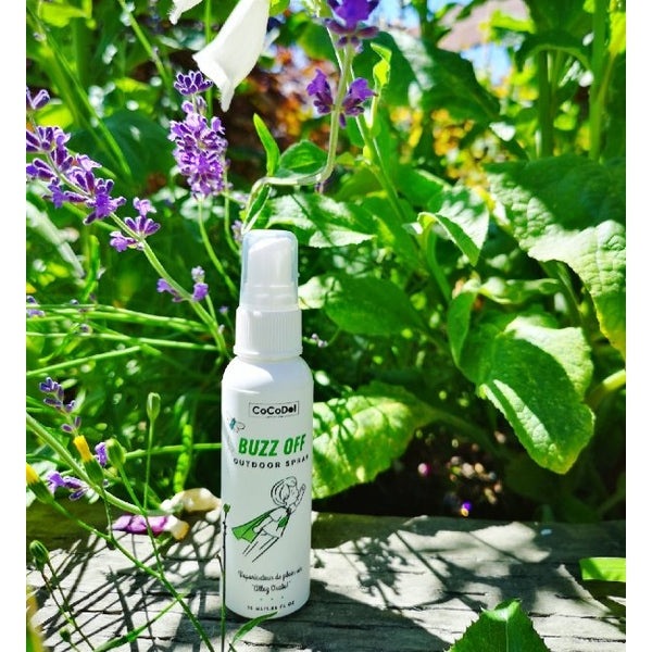 Cocodot Buzz-Off Outdoor Spray 55 ml white bottle with spray nozzle in a sunlit garden.