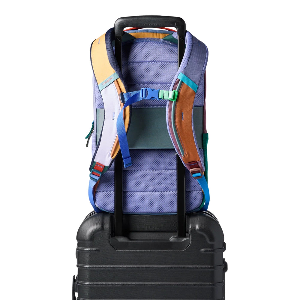 Cotopaxi Allpa 18L Daypack in multicolor purple with teal and orange straps on a rolling suitcase.