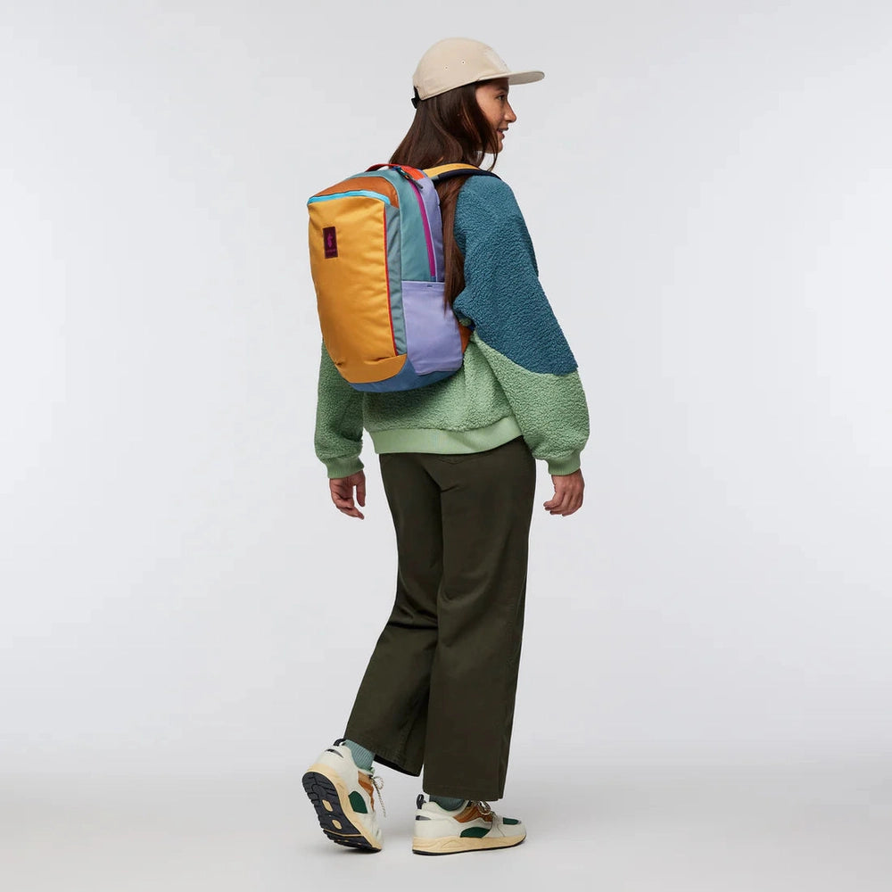 Cotopaxi Allpa 18L Daypack in multicolor patchwork (orange front, teal panels, lavender pocket) worn by model.