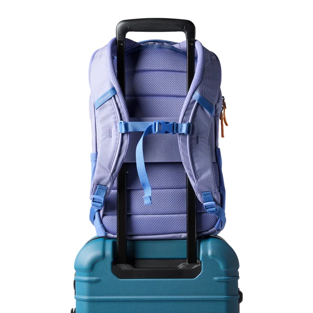 Cotopaxi Allpa 18L Daypack in lavender with blue straps mounted on a teal rolling suitcase
