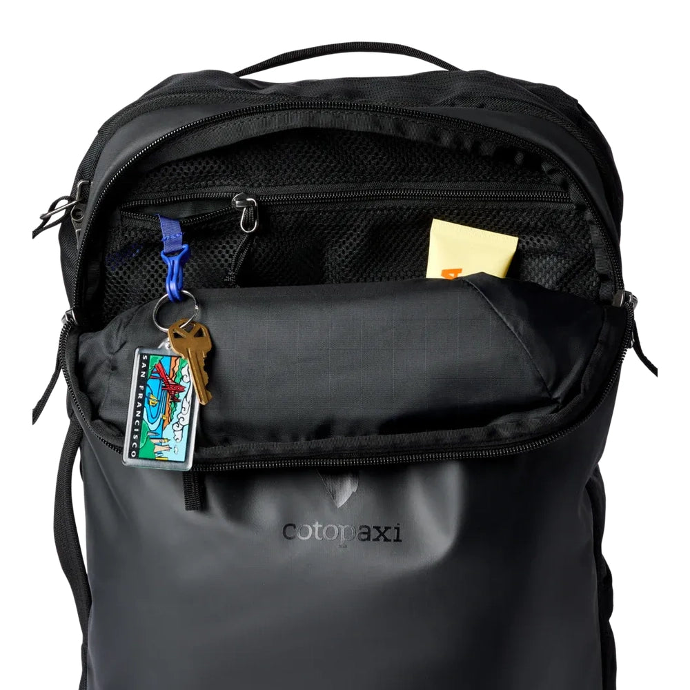 Cotopaxi Allpa 28L Travel Pack in Black with front zip pocket open, mesh pocket and keychain.