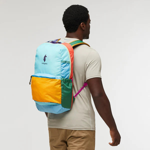 Cotopaxi Chiquillo 26L Daypack in light blue with orange front pocket and green side panel, worn by man in side view.