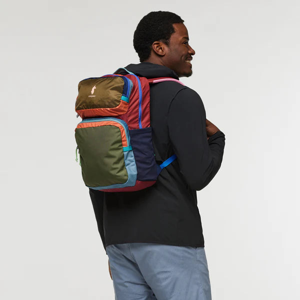 Cotopaxi Tasra 16L Backpack in multicolor patchwork with brown top pocket on man in black jacket (side view)