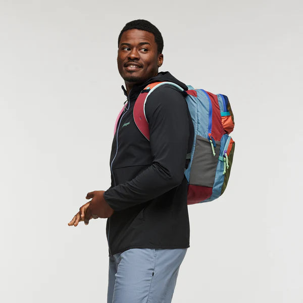 Cotopaxi Tasra 16L Backpack in patchwork with blue, red and orange panels, worn by man in black jacket side view.