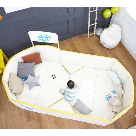Creamhaus Grand Ice Castle Up BT baby playpen with padded white panels and yellow trim, toddler playing inside.