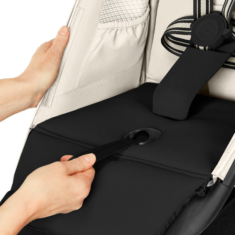 Cybex Avi Spin All Terrain Stroller: beige seat with strap being tightened to secure the child, harness ring visible.