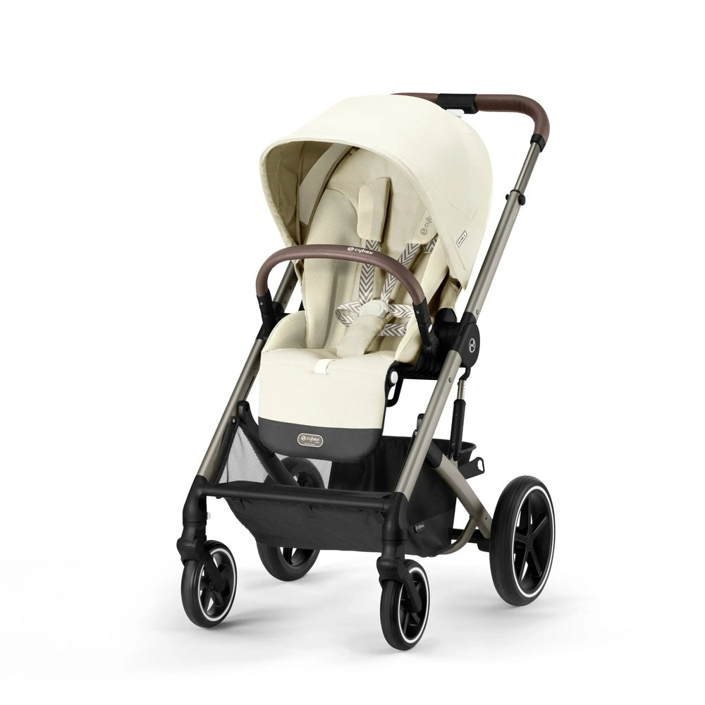 Cybex Balios S Lux stroller in beige with brown handlebar, extended canopy, and a securely strapped child in the seat.
