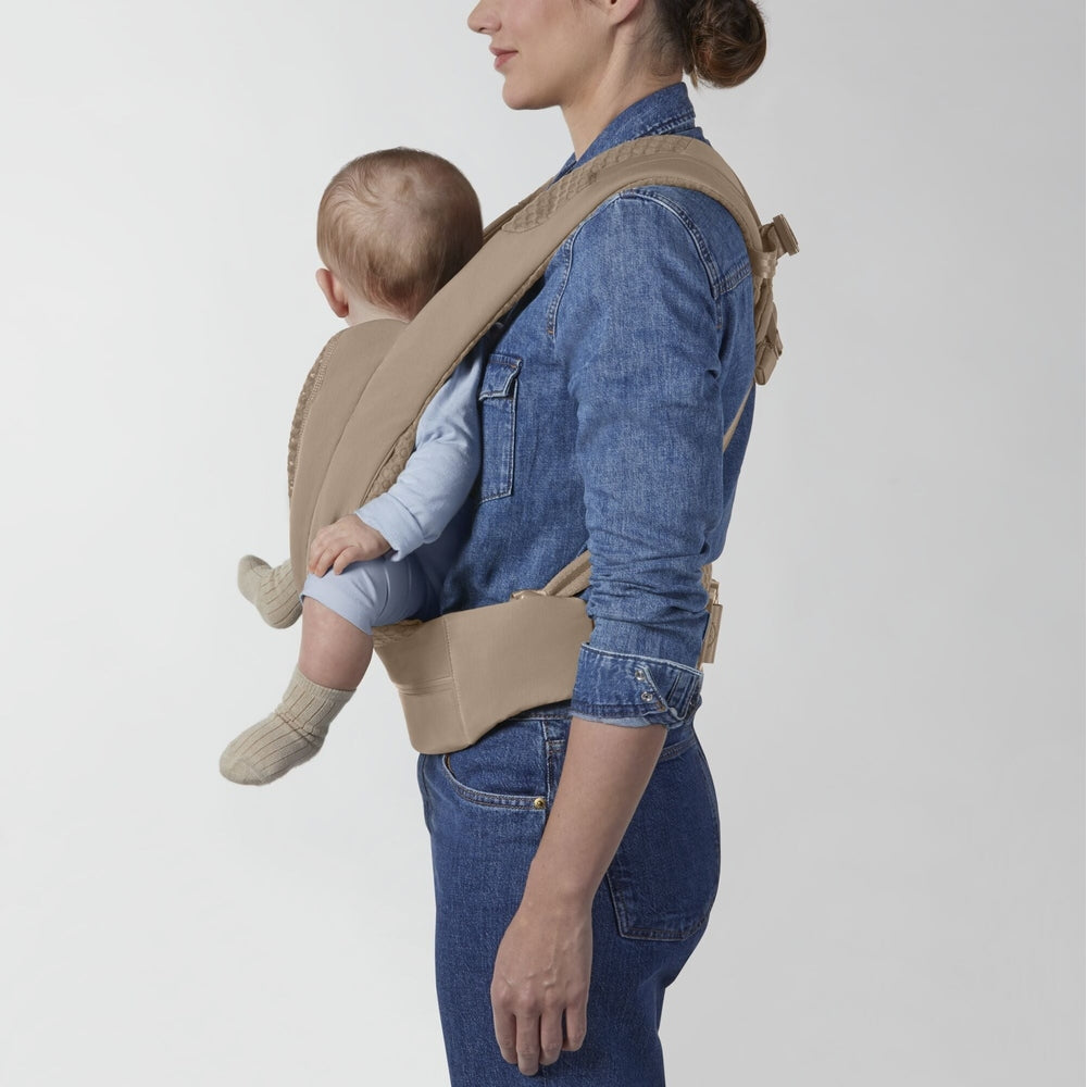 Beige fabric Cybex Coya baby carrier with padded straps worn over a denim shirt; infant in light blue.
