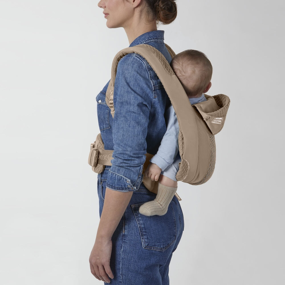 Beige quilted baby carrier on back with padded straps and waist belt; wearer in denim, baby in light blue onesie.