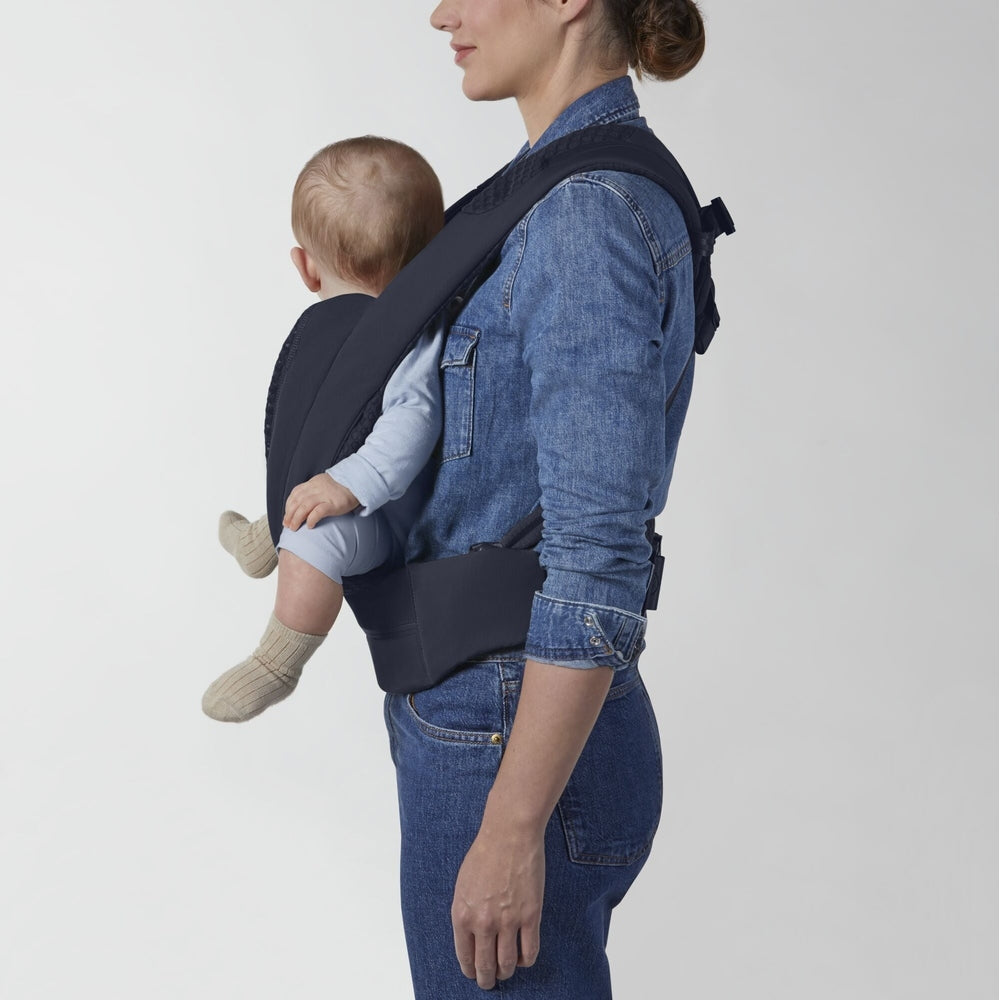 Dark navy Cybex Coya baby carrier with padded straps and wide waistband; infant in light-blue outfit inward-facing.