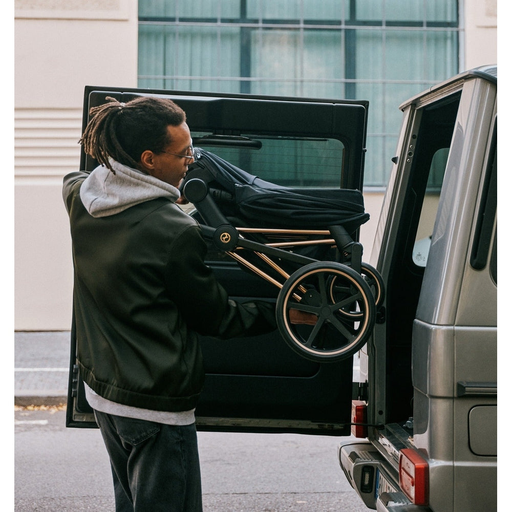 Cybex Priam 4 stroller in rose gold/sepia black with Lux Carry Cot, being loaded into a van