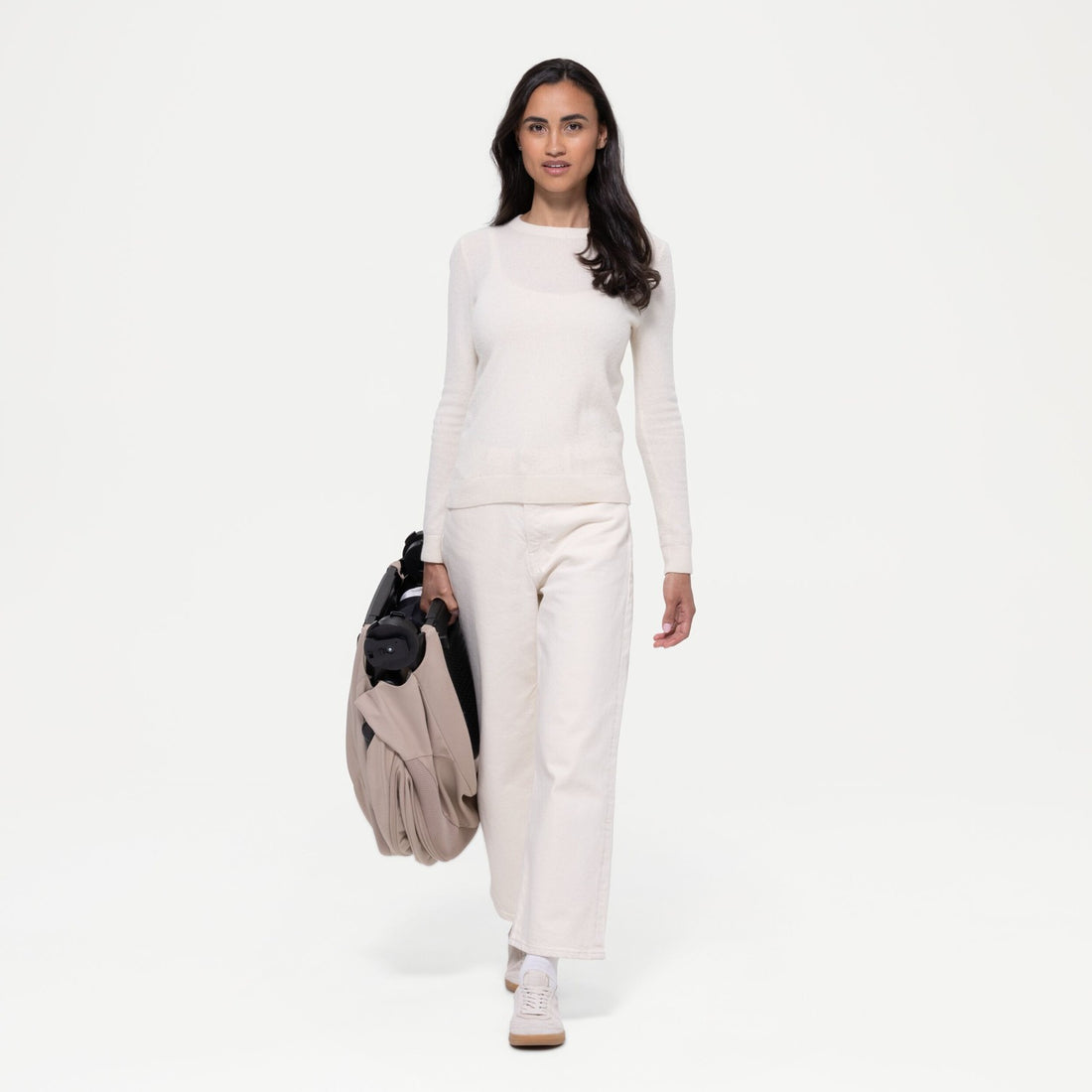 Woman carrying the folded Almond Beige Cybex Balios Fold Cot by its built-in handle
