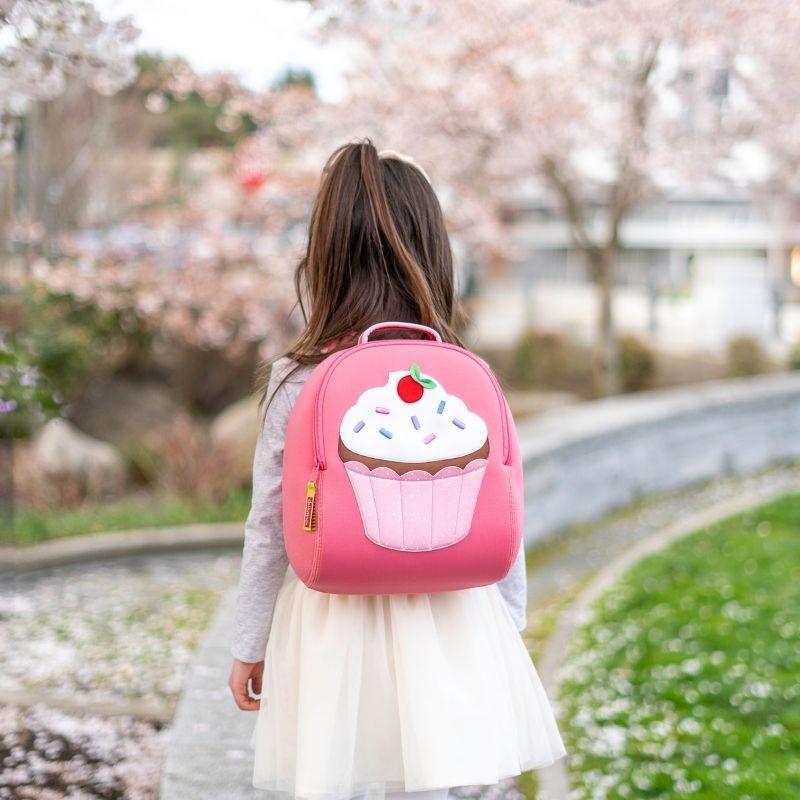 Dabbawalla cupcake toddler backpack in pink with frosting and sprinkles, worn by girl outdoors
