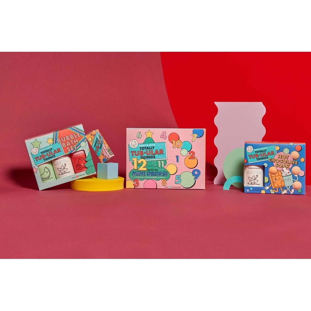 Dabble & Dollop 12 Days of Mini Drops Bath Bomb Countdown Calendar featuring bright, playful boxes arranged on a pink backdrop.