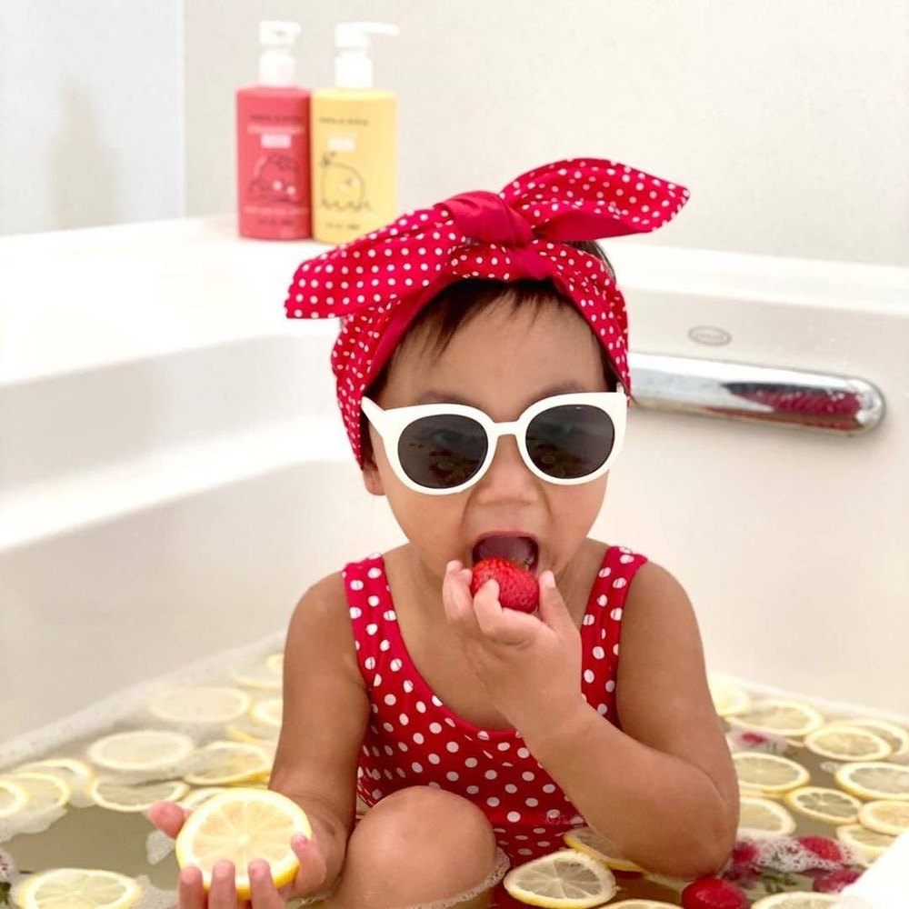 Dabble & Dollop All-Natural Shampoo, Body Wash & Bubbles Strawberry; child in red polka-dot outfit enjoys a strawberry bath.