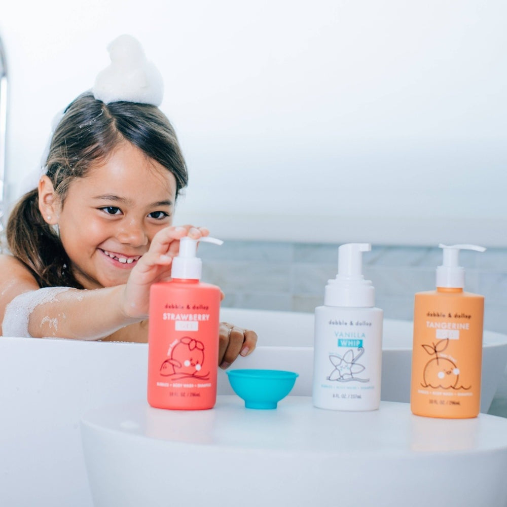 Dabble & Dollop All-Natural Shampoo, Body Wash & Bubbles Strawberry bottle held by a smiling girl in a bath.