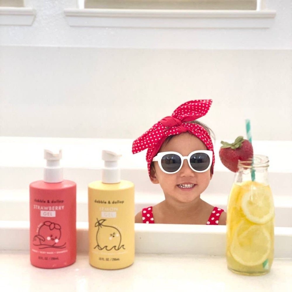 Dabble & Dollop All-Natural Shampoo, Body Wash & Bubbles Lemon; smiling toddler beside pink and yellow bottles in a bright bath.