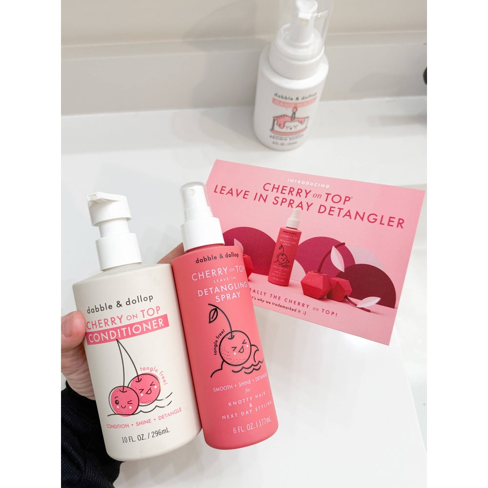 Dabble & Dollop Cherry on Top Detangling Spray & Conditioner set, pink spray bottle held beside white conditioner.