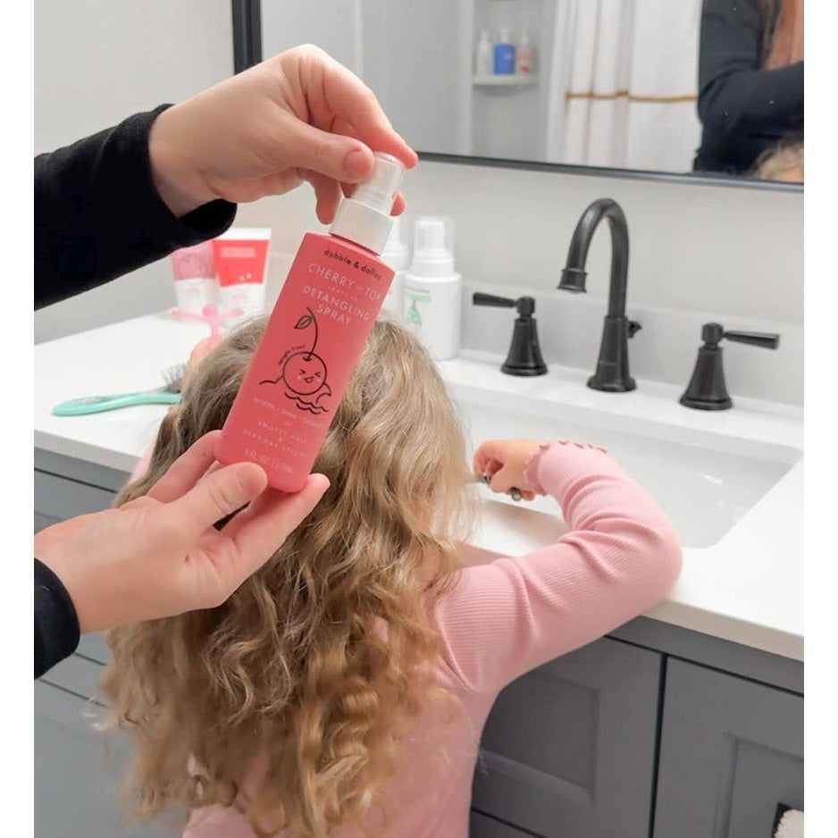 Dabble & Dollop Hair Detangling & Conditioning Spray Cherry on Top being sprayed onto a child's curly hair at the sink.