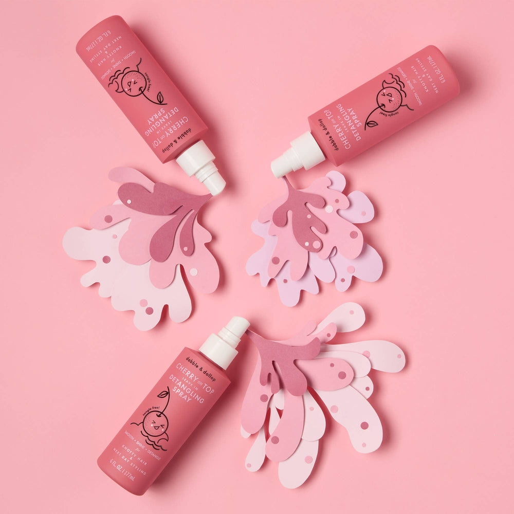 Dabble & Dollop Hair Detangling & Conditioning Spray Cherry on Top in pink bottle with spray nozzle among pink petal cutouts.