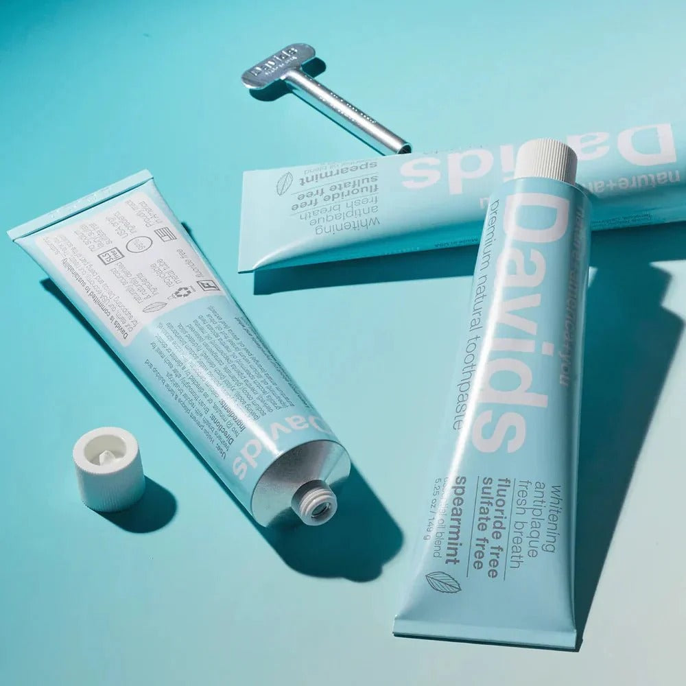 Davids Toothpaste Fluoride Free Spearmint tubes on turquoise surface, fluoride-free spearmint toothpaste with caps nearby.
