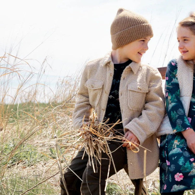 Deux Par Deux Sherpa Overshirt With Pocket Sesame on a boy holding dried grass in a sunlit field.