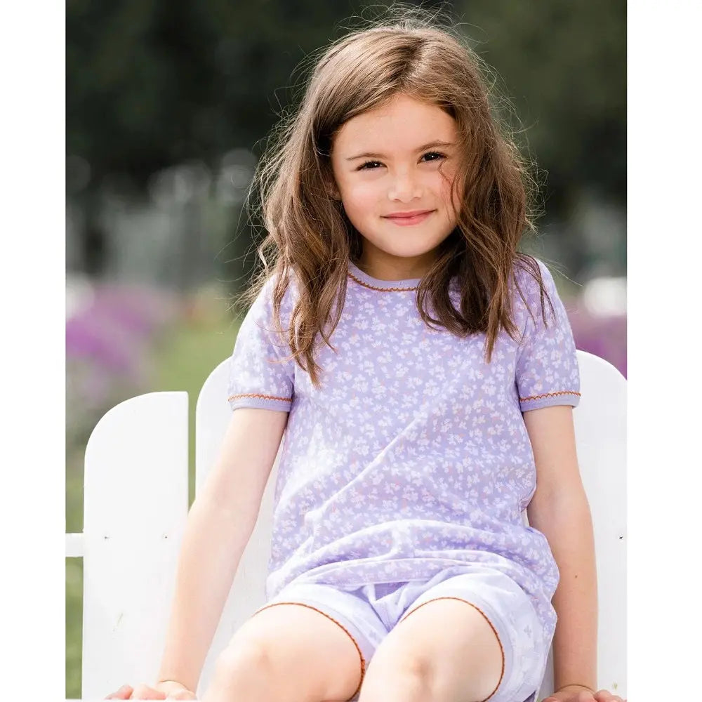 Deuxpardeux Organic Cotton Two Piece Pajama Set Lilac Printed Little Flowers, girl sits outdoors in lilac top and shorts.