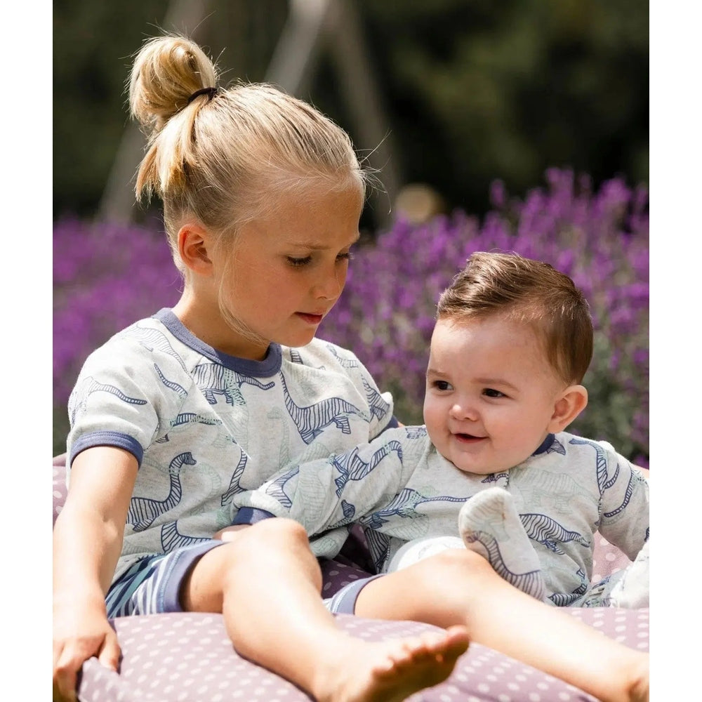 DeuxparDeux Organic Cotton Two Piece Short Pajama Set in heather beige with dinosaur print, siblings lounging in matching pajamas.