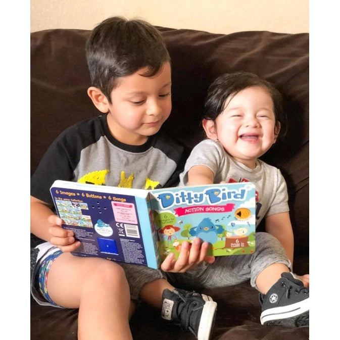 Two kids on a sofa happily read the Ditty Bird Sound Book Action Songs USB-C Rechargeable toy with a bright, colorful cover.