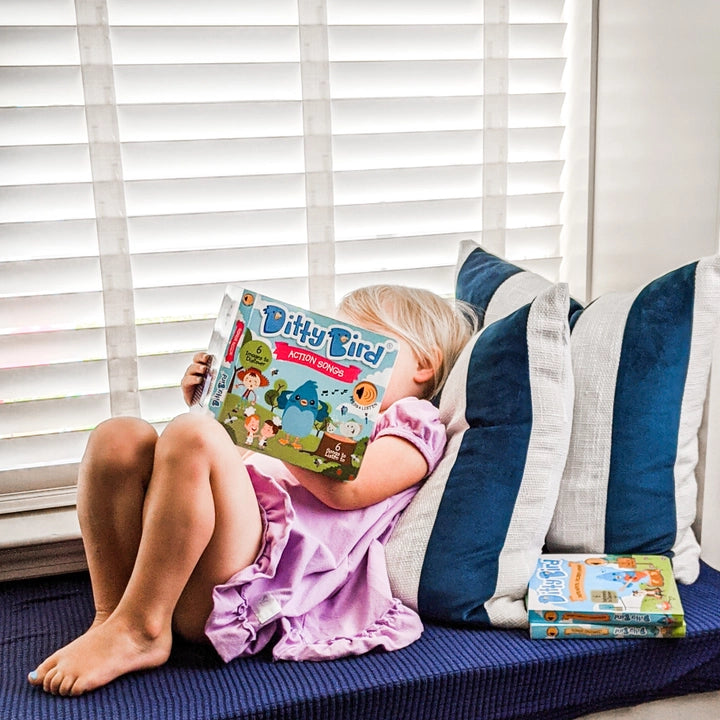 Ditty Bird Sound Book Action Songs USB-C Rechargeable; child sits on a blue cushion reading the colorful Ditty Bird book.