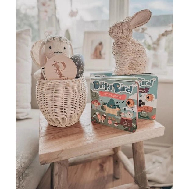 Ditty Bird Sound Book Action Songs USB-C Rechargeable toy on a sunlit table beside a woven bunny and basket.